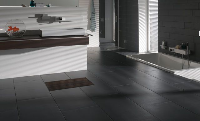 Foto: Deutsche Steinzeug Modernes Badezimmer mit dunklen Strukturfliesen, Badewanne, Waschtisch und Goldfischglas auf der Ablage.